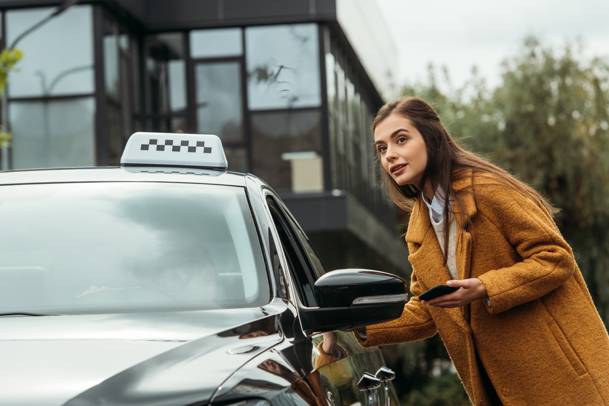Young woman with smartphone talking at taxi driver